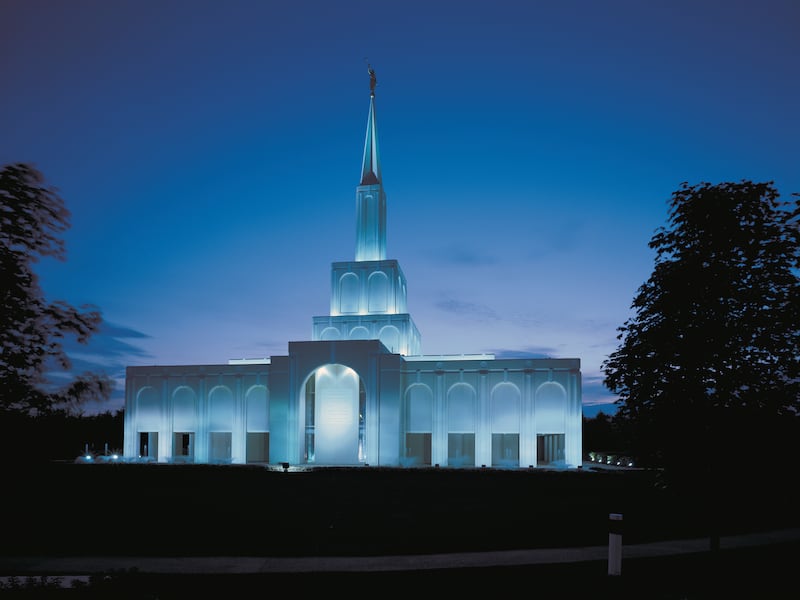 The Toronto Ontario Temple is a tiered single-spire temple with an Angel Moroni and has an entrance with a curved archway. It’s shown lit at twilight with blue skies fading to light purple.