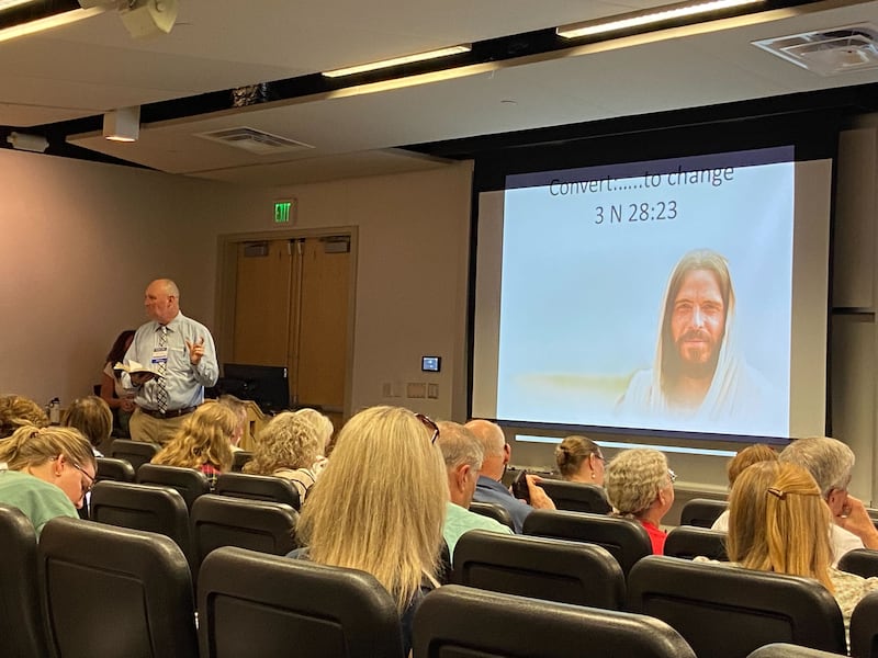 Gregory Johnson&nbsp;at the front of a lecture hall, standing next to a presentation slide with an image of the Savior and the words “Convert ... to change — 3 Nephi 28:23.”