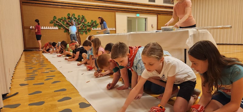 Primary children color on a large sheet of paper on the ground during the Marysville Washington Stake Primary day camp.