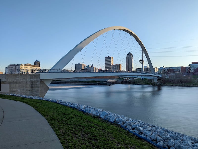 A bridge with an archway spans a review near the Des Moines, Iowa, downtown, with several high rise buildings in the background.