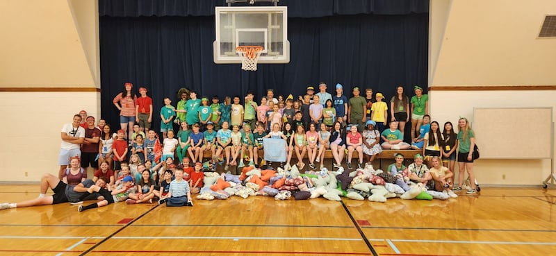 Dozens of Primary children, youth and teachers sit or stand around a stage with butterfly pillows they made for hospice patients during the Marysville Washington Stake Primary day camp.