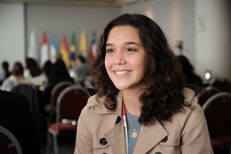 Martina Marcelino, wearing a tan coat, sits in a hotel conference room in Lima, Peru.