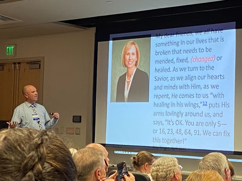 Gregory Johnson&nbsp;at the front of a lecture hall, standing next to a presentation slide with a quote from Sister Amy A. Wright about being changed by aligning one’s heart with the Savior.