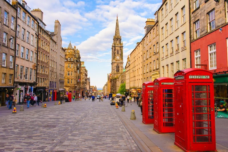 Red phone booths are on a cobbled street with a clock tower rising the back in Edinburgh, Scotland.