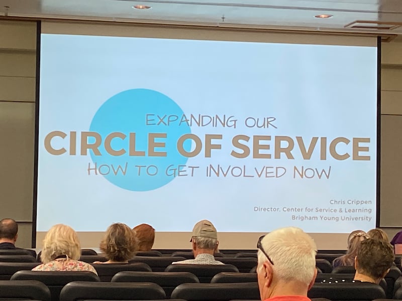 A presentation slide that says “Expanding Our Circle of Service” at the front of a lecture hall.