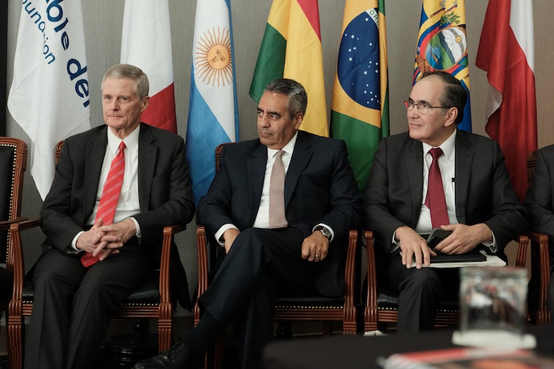 Elder David A. Bednar, Elder Jorge T. Becerra, and Elder Rafael E. Pino, are seated with flags behind them at El Roble's Seminario Sudamericano conference in Lima, Peru.