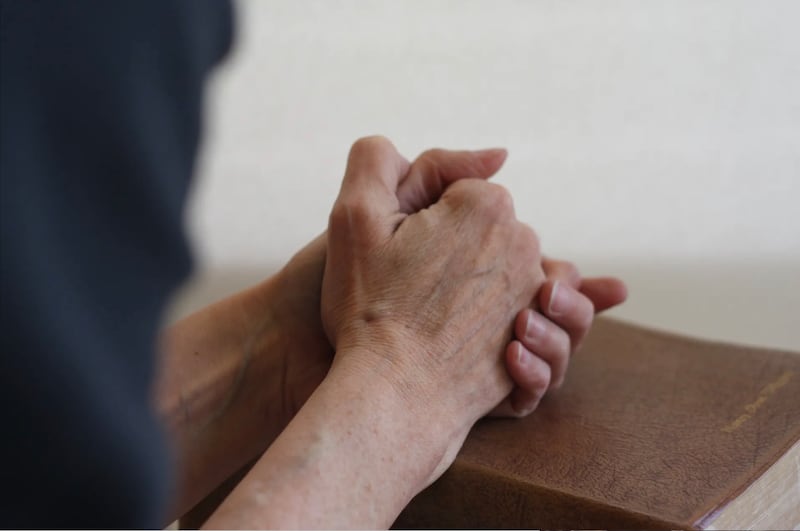 A person prays with clasped hands on scriptures.