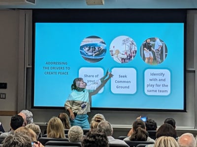 A woman points to a a projected image at the front of a classroom.