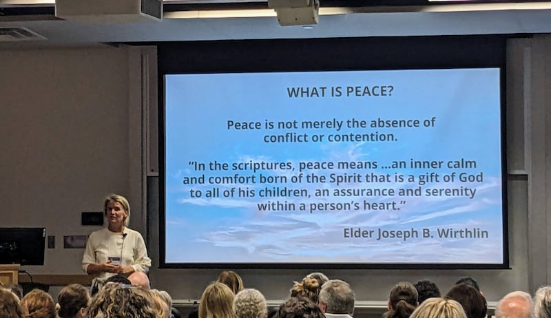 Emily de Schweinitz Taylor stands at the front of a classroom at BYU next to a screen that has several definitions of peace.